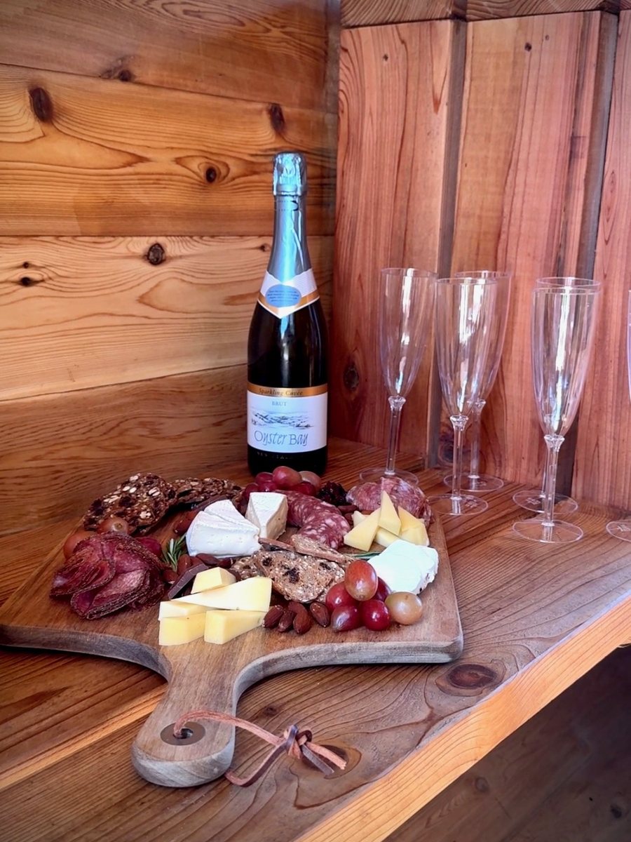 Charcuterie board and sparkling wine on a cedar bench inside the Wilderest mobile sauna