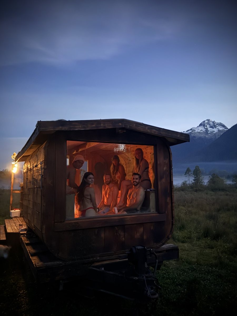 Friends in the Alpha wood-fired sauna at dusk with a snowy Sea-to-Sky mountain behind
