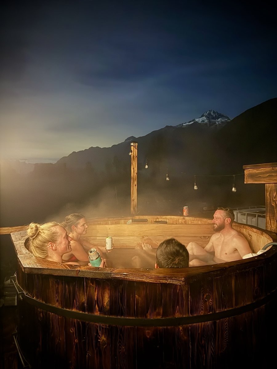 Friends in the steaming wood-fired hot tub at night with mountain views near Squamish