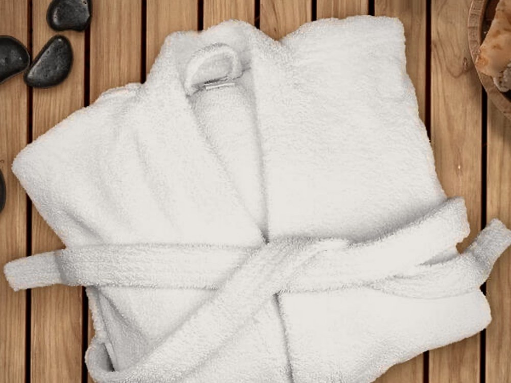 Folded white cotton spa robe on a cedar slat bench with black sauna stones